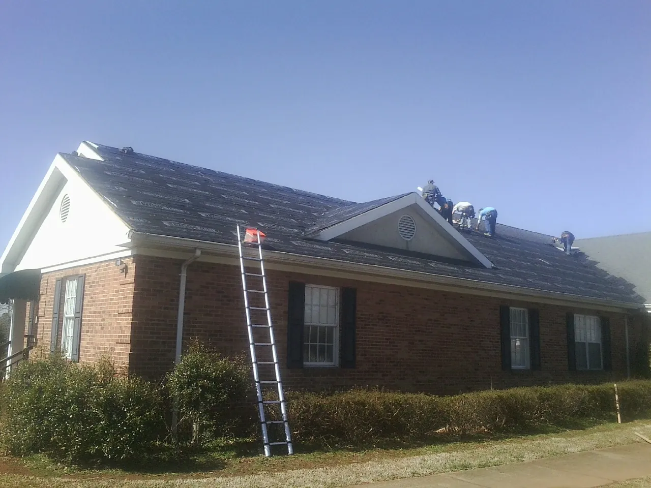Crew tearing shingles off a brick ranch roof with a ladder set — Metal Roof Repair work by our crew in Cerulean