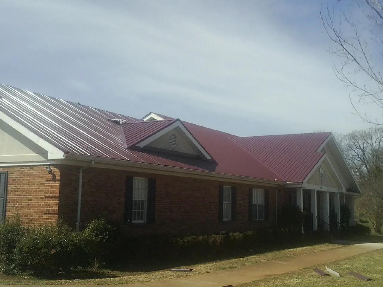 Red metal roof with gabled entries on a long brick building, from a Hail Damage Roof Repair job in Cerulean