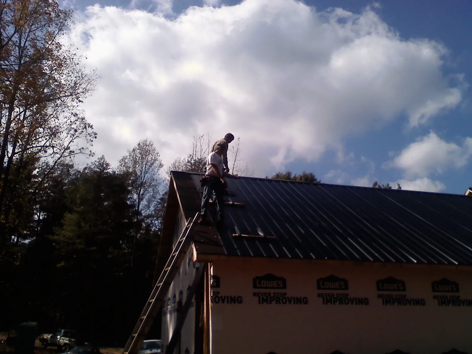 Roofer fastening dark metal panels high against a cloudy sky, from a Roof Inspection job in Cerulean