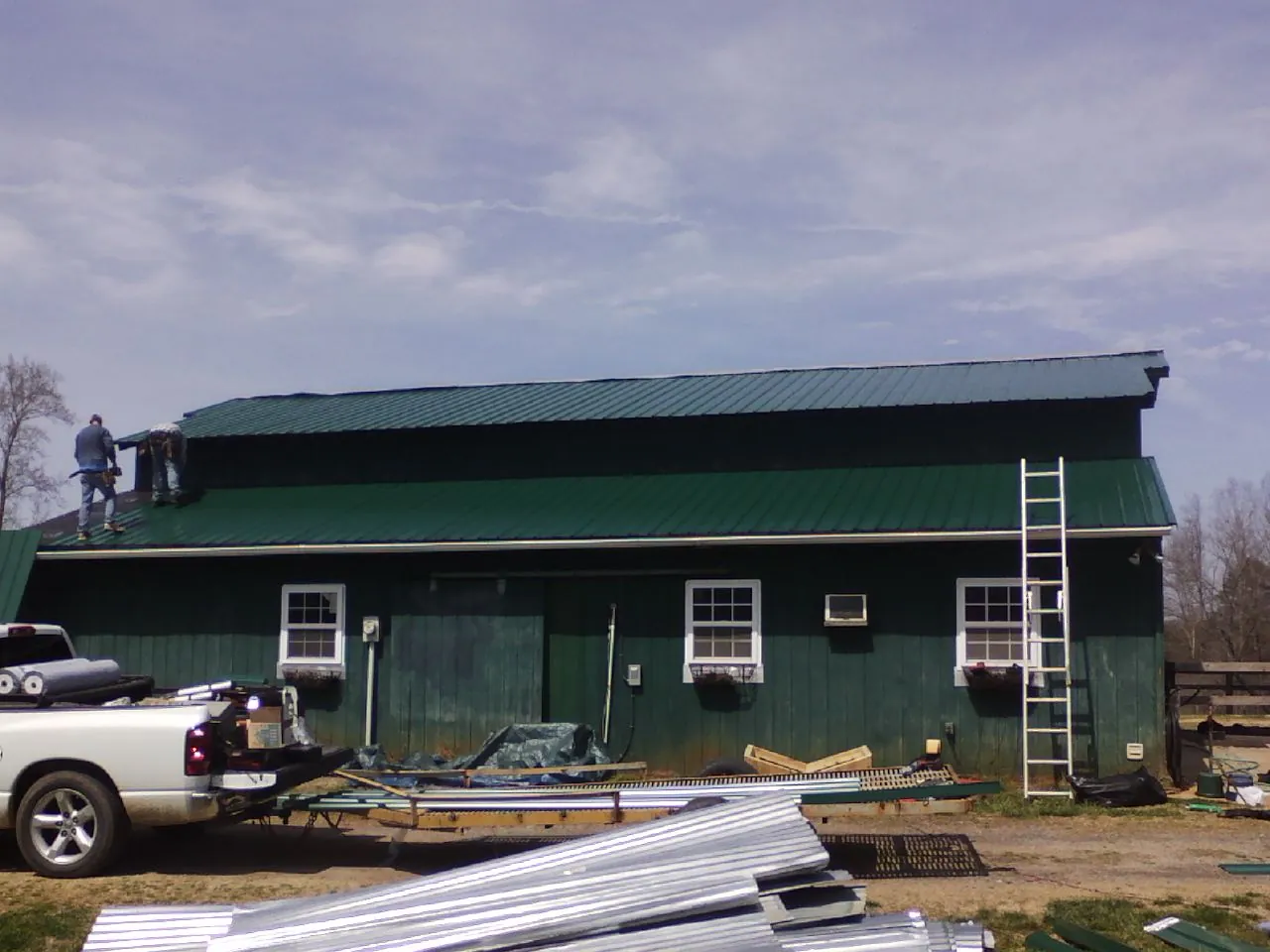 Crew installing green metal roofing on a large green barn in Cerulean